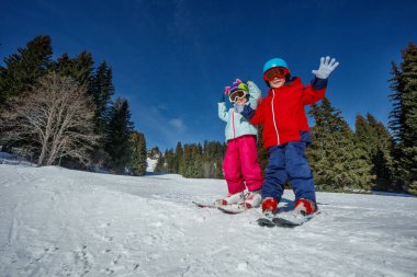 Kayak ve miğferlerle donatılmış bir çift genç, karla kaplı yamaçların, yüksek ağaçların, arka planda parlak mavi gökyüzünün tadını çıkarırlar.