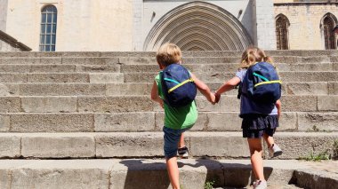 Bir erkek ve bir kız, küçük turistler el ele tutuşuyor, İspanya 'nın Girona kentindeki eski bir kilisenin yıpranmış merdivenlerinden çıkıyorlar.