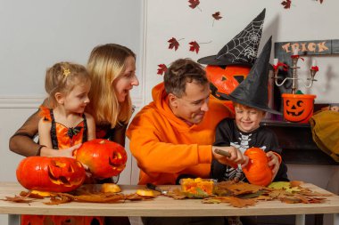 Sonbahar etkinliğinin tadını çıkaran bir aile Cadılar Bayramı için balkabaklarını oyuyor.