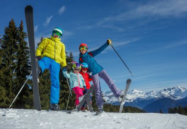 Renkli kayak kıyafetleri içinde, güneşli, karlı bir yamaçta dört kişi ayakta duruyor, kayakla bacaklarını kaldırarak maceraya hazır.