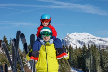 A child sits atop an adults shoulders, both warmly dressed for skiing, set against a stunning mountainous backdrop clipart