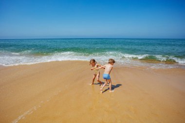 İki çocuk, bir oğlan ve bir kız okyanusun kıyısında dans ediyorlar, gülüyorlar, kumda yalınayak koşuyorlar.
