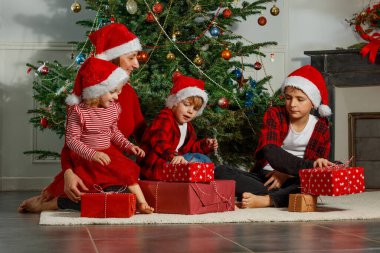 Mutlu bir aile Noel ağacının etrafında toplanıyor. Bir kadın ve iki çocuk mutlu bir şekilde hediyelerini açıyor.