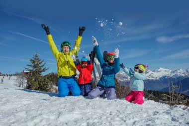 Bir grup çocuk ve ebeveyn kayak tatillerinde eğleniyorlar güneşli bir günde açık mavi gökyüzüne kar atıyorlar.