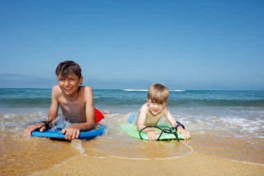 İki çocuk sahilde vücutlarında süzülen dalgaların heyecanını kucaklıyor.