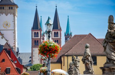 Almanya, Bavyera 'da parlak mavi gökyüzünün altında yüksek kilise kuleleri, dekoratif çiçekler ve heykellerle dolu Wurzburg' un güzel bir manzarası.