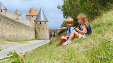 Fransa 'nın Carcassonne kentindeki eski bir şatonun yakınındaki çimenli bir yamaçta oturan iki genç çocuk turist tatillerinin tadını çıkarıyorlar.