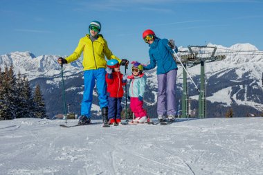 Dört kişilik bir grup, iki çocuklu aileler güneşli bir kış gününde karlı dağlarda kayak yapıyor.