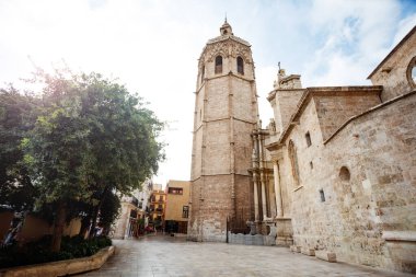 Antik tuğla çan kulesi Micalet, açık gökyüzünün altında dikiliyor. Etrafı yeşil yapraklarla çevrili ve İspanya, Valencia 'da asfalt bir meydan.