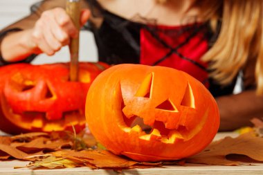 Bir insanın elleri bıçakla balkabağını keserken görülüyor. Kuru yapraklar etrafa saçılmış.