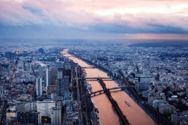 Paris gökyüzü bulutlarla dolu kasvetli bir günbatımı altında uzanır. Birden fazla köprüsü olan Seine Nehri merkezde.