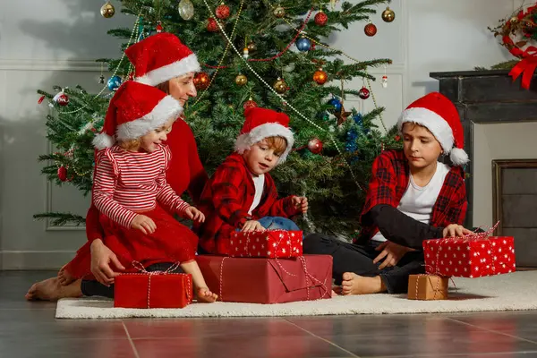 Mutlu bir aile Noel ağacının etrafında toplanıyor. Bir kadın ve iki çocuk mutlu bir şekilde hediyelerini açıyor.