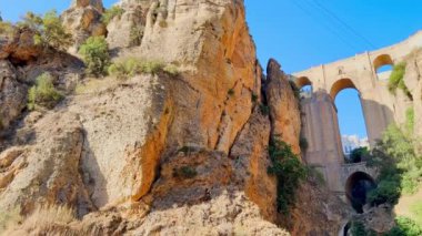 Görkemli bir taş köprü Puente Nuevo, İspanya 'nın Ronda kentindeki açık mavi gökyüzünün altında kayalık uçurumlar ve seyrek yeşilliklerle çevrili derin bir vadiyi kaplar.