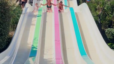 Üç kişi, anne ve iki çocuk deniz kenarında yaz tatili sırasında su kaydırağının keyfini çıkarıyorlar. 