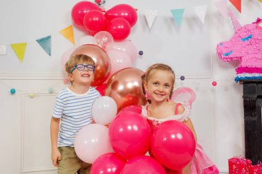 Kardeşler, oğlanlar ve kızlar bir sürü pembe doğum günü balonu tutarlar, gülümserler, doğum günü partilerine gülerler.