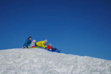 Çocuklar ve iki ebeveyn açık havada karlı bir tepede kızak kayıyor, kış tatilleri eğlenceli mavi gökyüzü fotokopi alanı yukarıda