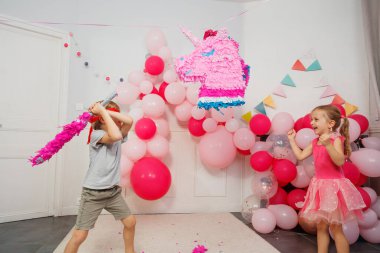 Bir pinataya vurmaya hazırlanan gözleri bağlı bir genç, bir parti etkinliğinde pembe kıyafetli bir kız tarafından alkışlanır.