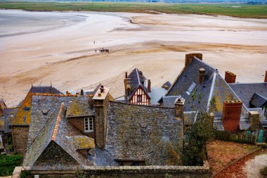 Tarihi bir kasabanın çatıları geniş bir kumlu alanın zeminine karşı duruyor. Uzak gruplar sahneye hayat katıyor.