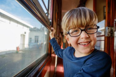 Gözlüklü bir çocuğun komik bir portresi. Eski trenin içinde, aile gezisinde bol bol gülümsüyor.