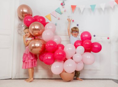 Peri gibi giyinen kız, balonlarla etkileşime giriyor. Çizgili tişörtlü oğlan kolunu kaldırıyor.