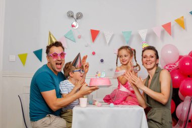 Bir partide bir araya gelen aile, pembe pasta ve canlı süslemelerle dolu bir doğum gününü coşkuyla kutluyor.