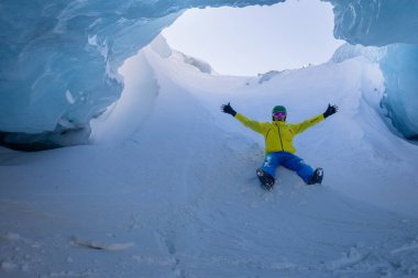 Buzul mağarasında yatan sarı giysili bir insan kollarıyla heyecan sergiliyor.
