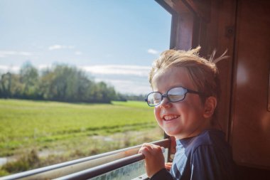 Mutlu küçük çocuk öne doğru eğiliyor, gözleri yuvarlanan tarlalarda, ağaçlık arazilerde ve uzak tepelerde yaz tatili yolculuğunda.