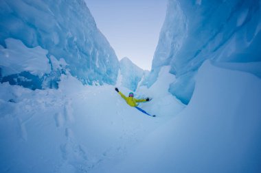 Buz gibi uçurumların ortasında, parlak giyinmiş yetişkin bir adam kutlama için kolunu kaldırıyor.