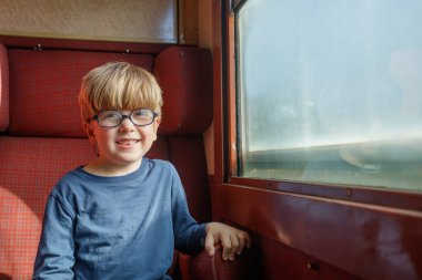 Sevimli çocuk bir kolu koltukta dinleniyor, yaz tatili boyunca trenle seyahat etmekten mutlu.