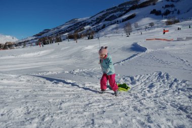 Bir çocuk, açık mavi bir gökyüzünün altında, Fransa 'da Noel tatillerinde neşeli bir şekilde kızağı sürüklüyor.