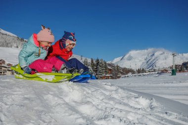 İki kardeş bir kızağı paylaşıyor, karların üzerinde süzülüyorlar kar kaplı dağların ötesinde.
