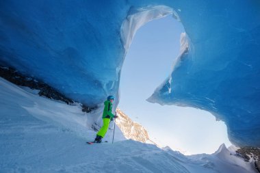 Kasklı ve parlak kıyafetli kayakçı genç, kalp şeklindeki girişten kayak yaparak buzul mağara oluşumlarını keşfediyor.