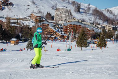 Yeşil kayak takımındaki bir çocuk kır evlerinin yakınındaki karlarda geziniyor tatillerde iyi eğlenceler.