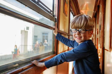 Mavi kazaklı bir çocuk kameraya doğru dönüyor, arabanın güneş ışığı altındaki raylar boyunca tıkırdaması gibi geniş bir gülümsemeyle.