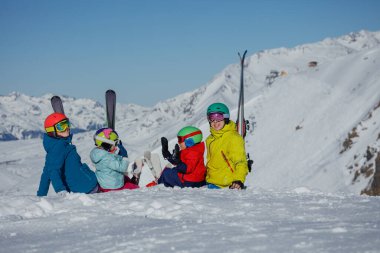Parlak gün ışığı altında, bir aile babası baba oğul ve kız renkli kayak kıyafetleri giyer ve karlı dağ manzarasını birlikte keşfederler.
