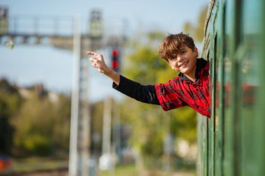 Mutlu genç, aile gezisinde hareket halindeki tren penceresinden eğilip el sallıyor.