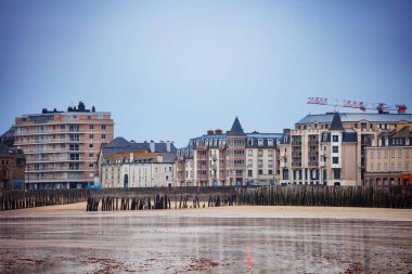 Sahil şeridi, önünde geniş bir kumlu alan ve bulutlu bir zemin, Saint-Malo, Bretagne, Fransa ile birlikte tarihi yapılarla işaretlenmiştir.