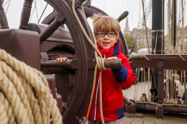 Çocuk gülümsüyor ve büyük bir tekerin arkasında duruyor. Deniz müzesini keşfetmek için heyecanlı.