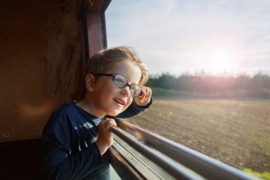 Öğleden sonra güneşi tarlalarda ve çitlerin arasında sıcacık bir ışık saçarken sırıtarak açık pencereden dışarı sarkmış.