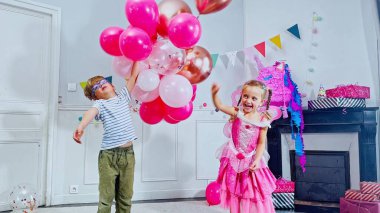 Bir çift çocuk doğum günü kutlamasıyla mutlu olurlar, parlak pembe balonlarla oynarlar, zıplarlar, kaldırırlar, eğlenirler.
