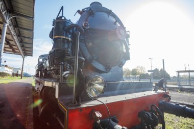 Motorun yüzü güneşte parlıyor, buhar delikleri kıtır kıtır öğlen havasında usulca tıslıyor.