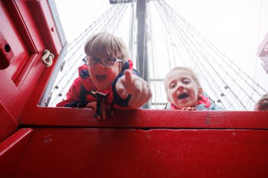 Heyecanla, grev ceketli iki çocuk kırmızı bir teknenin kenarından dışarı bakıyorlar, ilginç bir turistik cazibe.