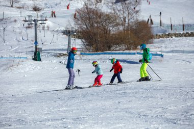 Bu karlı ortamda, bir kayak koçu üç genç öğrenciyi, parlak giysileriyle tepeden aşağı doğru yönlendirecek.