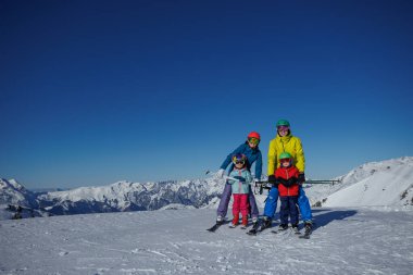Karda canlı bir gün, dört kişilik bir ailenin ufukta yükselen dağlarla kayak yaptığını görür.