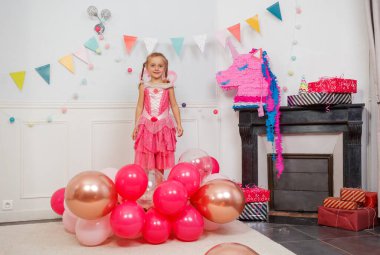 Neşeli bir şekilde gülümseyen, peri elbiseli genç bir kız, festivalde renkli balonlarla poz veriyor.