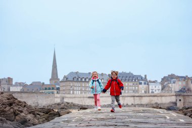 Bir çift çocuk sevinçle kaldırım boyunca koşuyor tarihi mimarisi ve arkadaki kayalık sahili ile Saint-Malo, Bretagne, Fransa