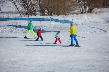 Dört kişilik bir grup, yetişkin eğitmen geriye doğru kayıyor ve çocuklar, karlı bir yamaçtan birlikte kayıyorlar.