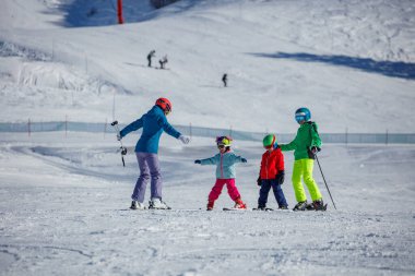 Koç, Alp Tatil Köyü 'nde karlı bir yamaçta birlikte gezinen bir grup çocuğa kayak dersi veriyor.