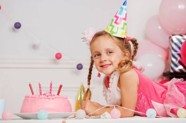 Parlak bir şekilde gülümseyen çocuk, canlı bir dekorun ortasında yanan mumlarla süslenmiş pastasına hayran kalıyor.