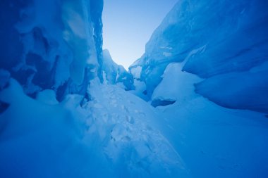Kutup bölgesinin görkemli ve ürpertici cazibesinin altını çizen dev mavi buz uçurumlarının arasında karla kaplı bir yol.